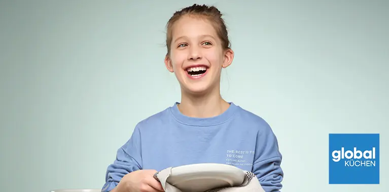 Person im blauen Sweatshirt trocknet weissen Teller mit Geschirrtuch vor Tellerstapel, unten rechts blaues Logo mit Schriftzug global Küchen.